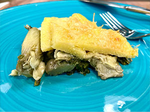 Baked artichoke and spinach polenta served on a blue dish.